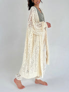 Woman wearing a long, light-colored crochet cardigan on a plain background