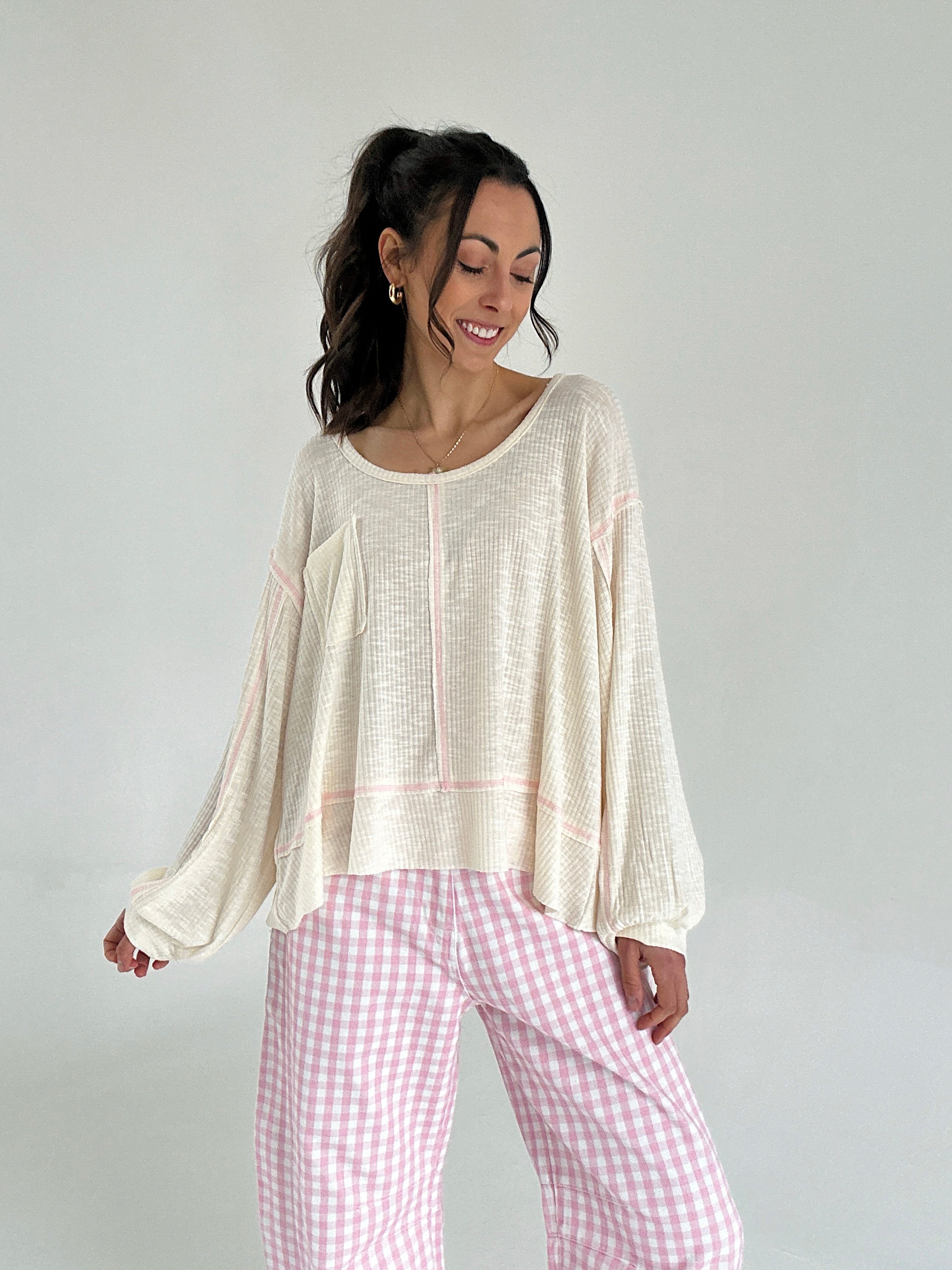 Woman wearing a beige top and pink checkered pants against a plain background