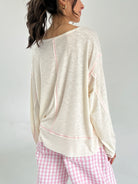 Woman wearing a beige long-sleeve top and pink checkered pants on a plain background from back