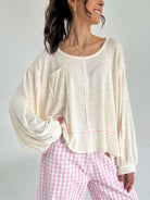 Woman wearing a cream-colored top and pink checkered pants on a plain background