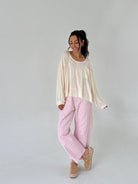 Woman wearing a cream sweater and pink checkered pants on a plain background