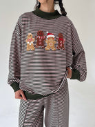 A person wearing a horizontally striped long-sleeve sweatshirt with a festive gingerbread man graphic across the chest, paired with matching striped pants. The garment features solid dark olive green ribbed mock neck, cuffs, and hem.