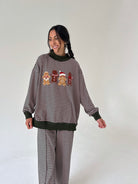 A woman modeling a matching holiday-themed sweatshirt and sweatpants set. The set features thin horizontal stripes with solid dark brown ribbed trim at the crew neck, cuffs, and hem.