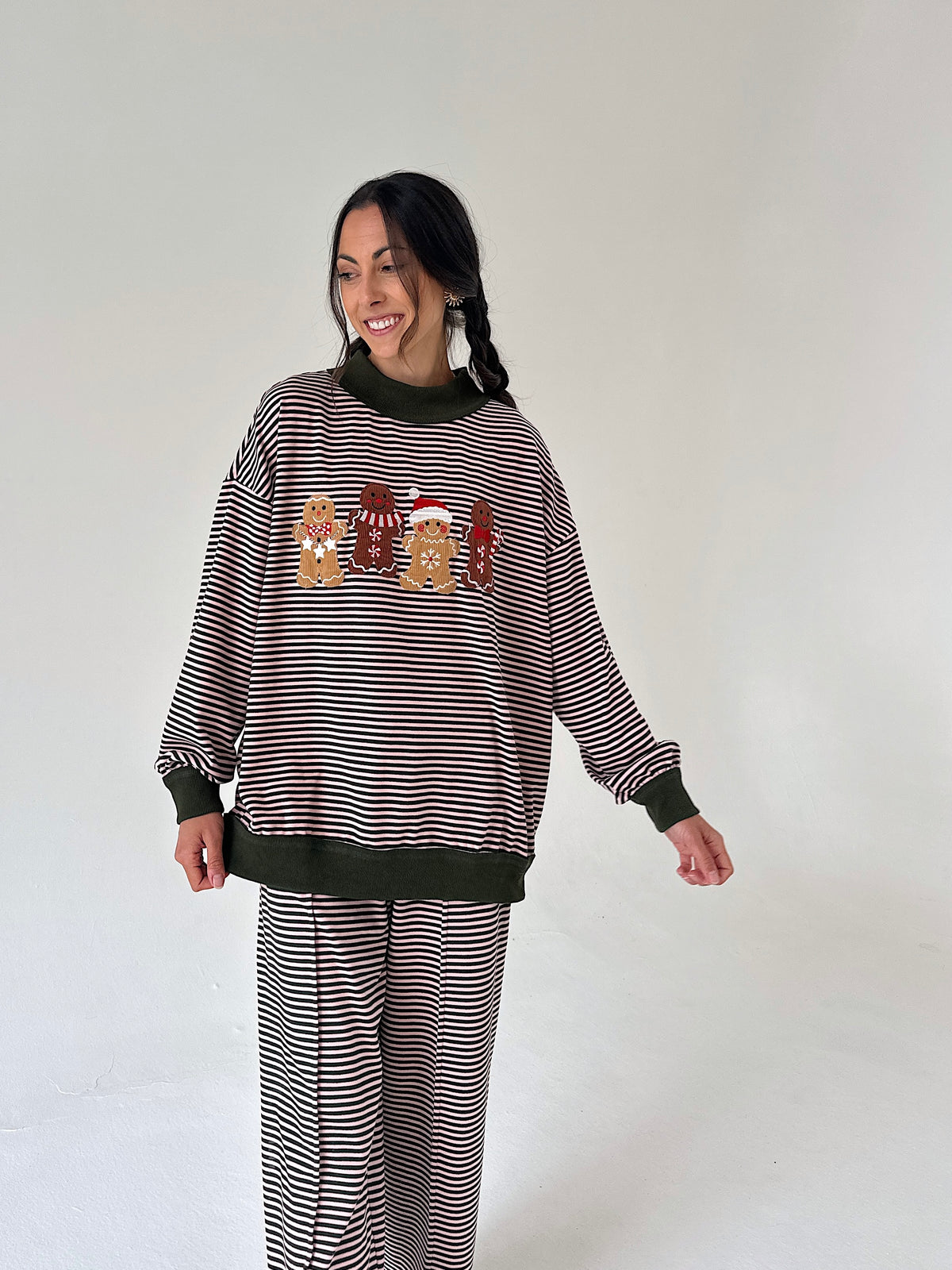 A woman modeling a matching holiday-themed sweatshirt and sweatpants set. The set features thin horizontal stripes with solid dark brown ribbed trim at the crew neck, cuffs, and hem.