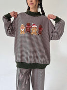 A woman wearing a matching holiday pajama set with horizontal stripes, dark green ribbed trim, and a gingerbread-themed graphic on the front.
