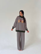 A woman modeling a matching two-piece loungewear set consisting of a long-sleeve sweatshirt and wide-leg pants. The set features horizontal stripe pattern with a small colorful graphic on the chest.