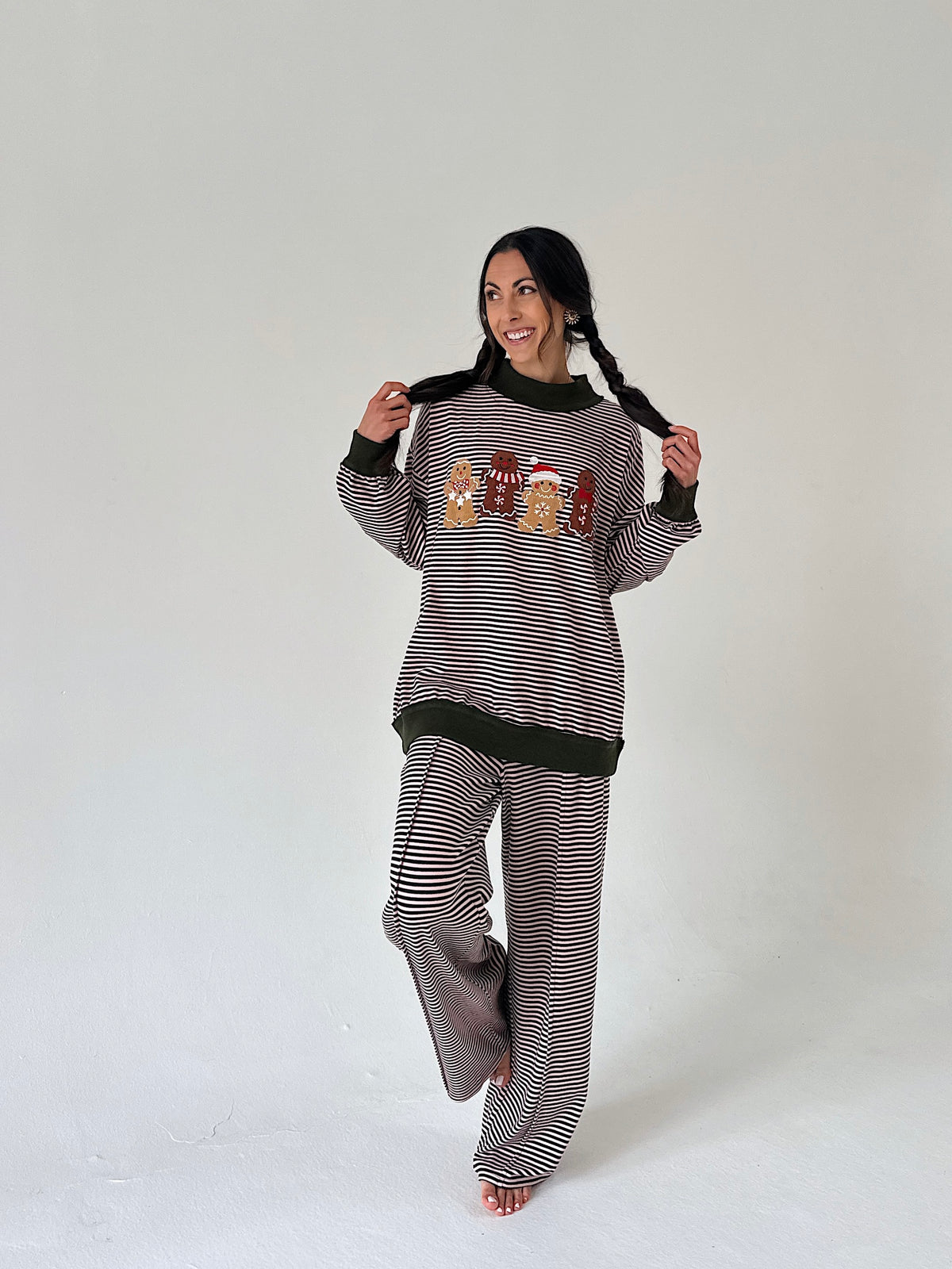 A woman modeling a matching two-piece loungewear set consisting of a long-sleeve striped sweater and wide-leg pants. The set features thin horizontal stripes, solid black ribbed trim at the collar, cuffs, and hem, and a central graphic of three cartoon characters wearing red hats.