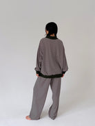A person shown from the back wearing a matching striped lounge set consisting of a long-sleeve top and wide-leg pants, photographed against a plain light gray studio background.