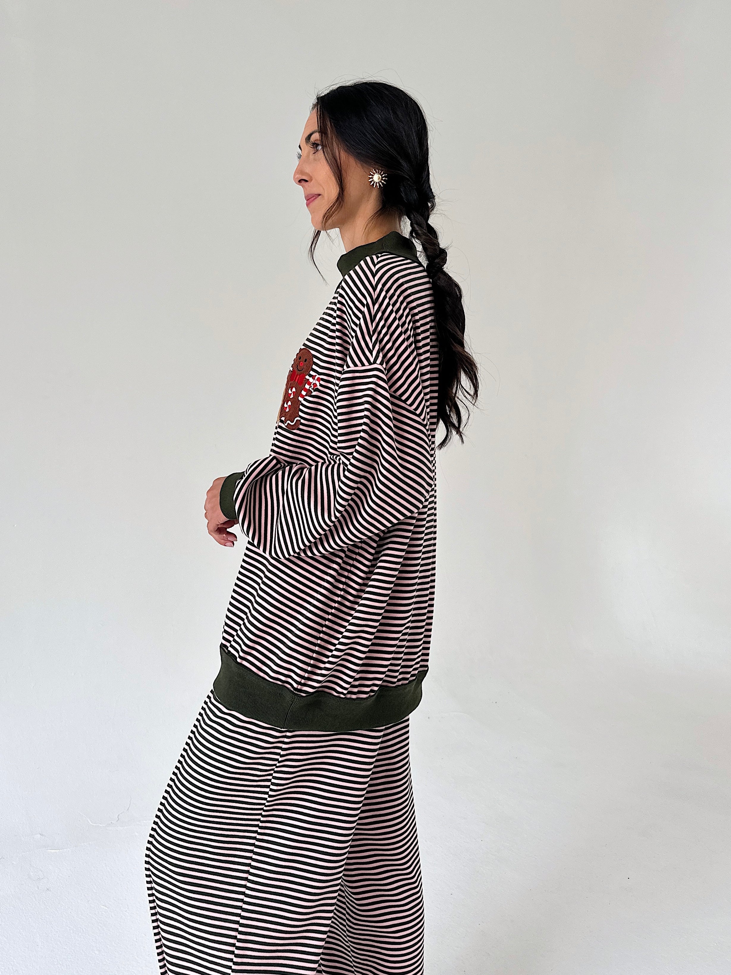 A woman in profile wearing a matching striped lounge set with dark green ribbed trim, including a long-sleeve top and wide-leg pants, against a plain light gray studio background.