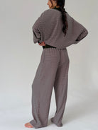A woman shown from the back wearing a matching two-piece loungewear set with horizontal stripes, consisting of a long-sleeve top and wide-leg pants, against a plain light gray studio background.