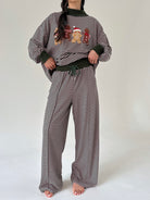 A person modeling a matching holiday-themed lounge set consisting of a long-sleeve top and wide-leg pants. The set features a horizontal stripe pattern, dark green ribbed collar, cuffs, and drawstring waist, and gingerbread men graphics on the chest.