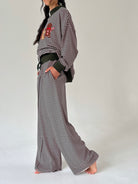 A model wearing a striped long-sleeve top and matching wide-leg pants, styled with a dark green belt and a red embroidered patch on the chest, set against a plain light gray background.