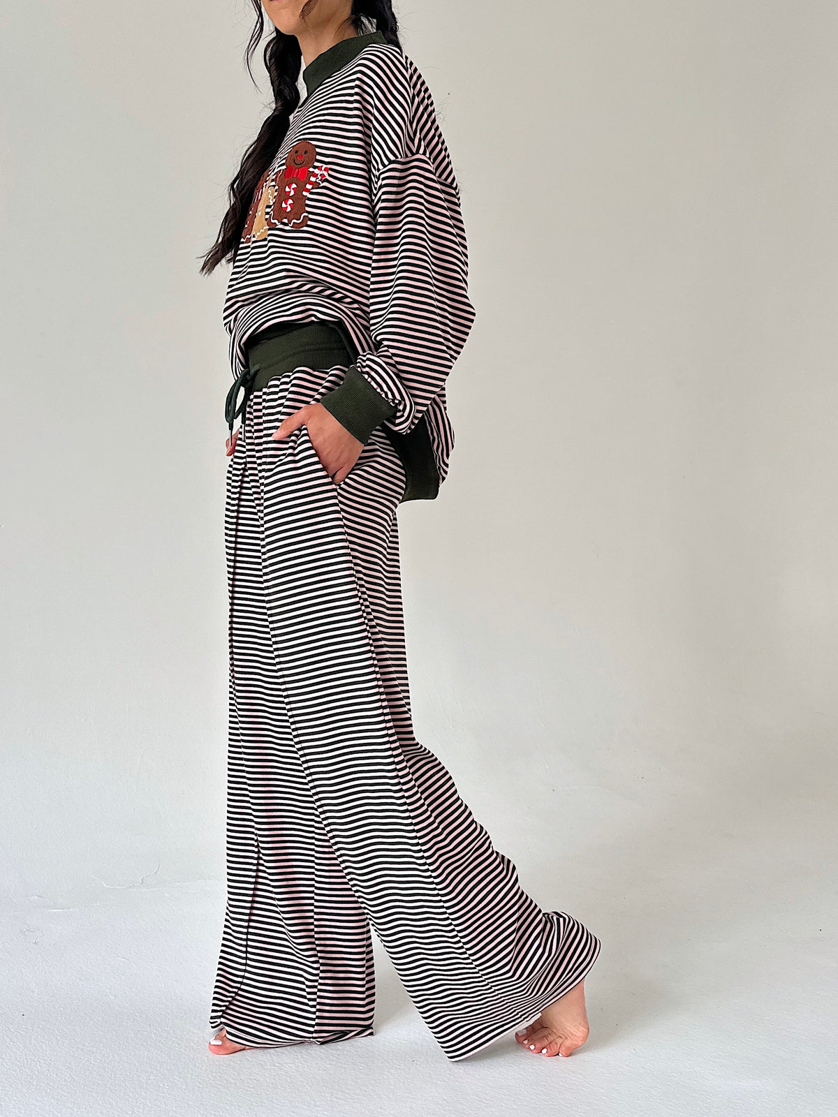 A model wearing a striped long-sleeve top and matching wide-leg pants, styled with a dark green belt and a red embroidered patch on the chest, set against a plain light gray background.