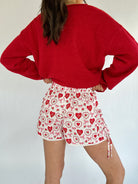Person wearing a red sweater and patterned shorts on a plain background