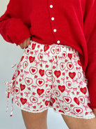 Person wearing a red cardigan and white shorts with red heart and bow pattern on a light gray background