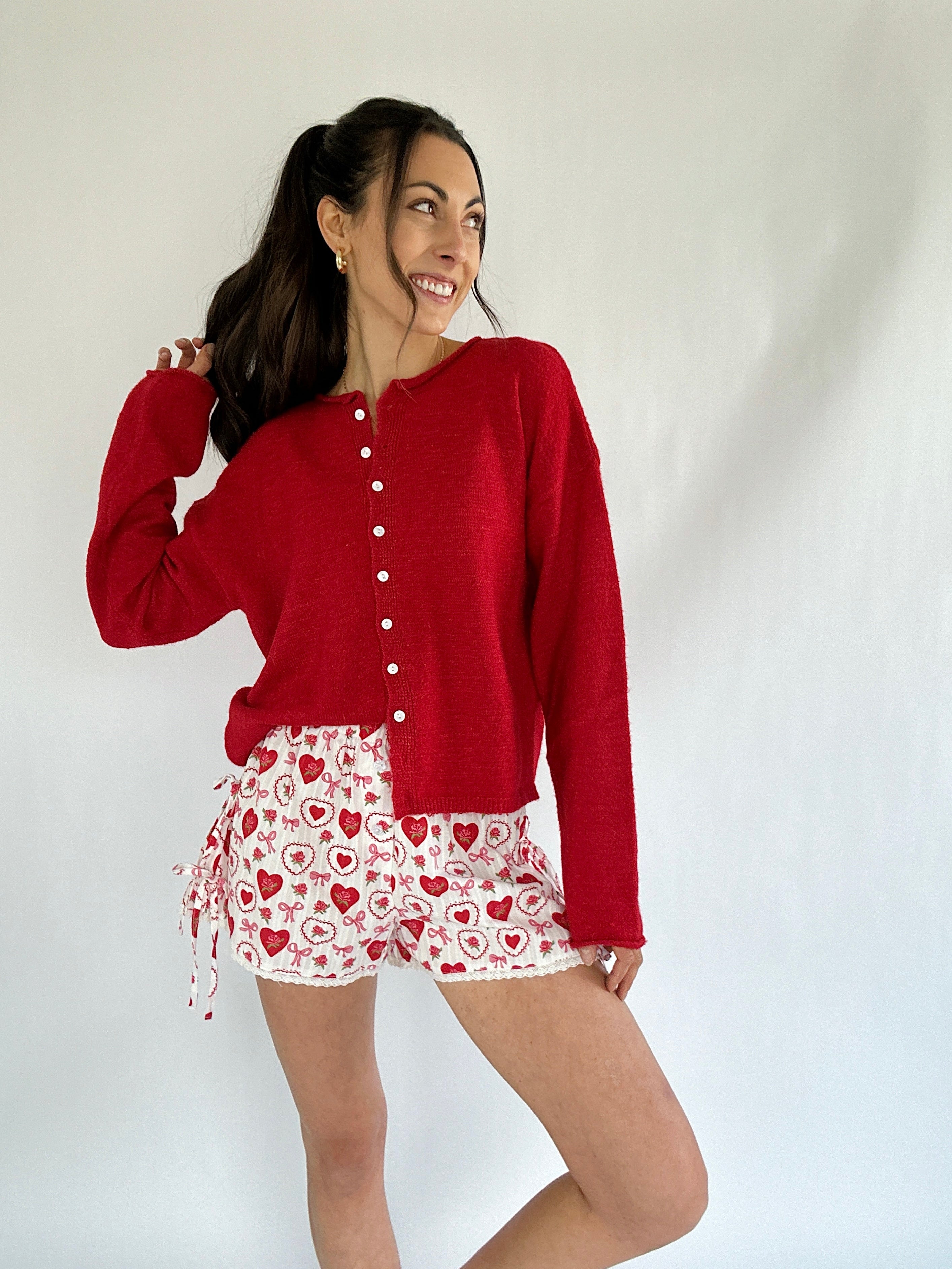 Woman wearing a red cardigan and heart-patterned shorts on a white background