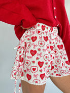Person wearing a red cardigan and a white shorts with red heart and bow pattern showing side tie details