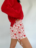 Person wearing a red cardigan and white shorts with red heart patterns on a plain background showing side details