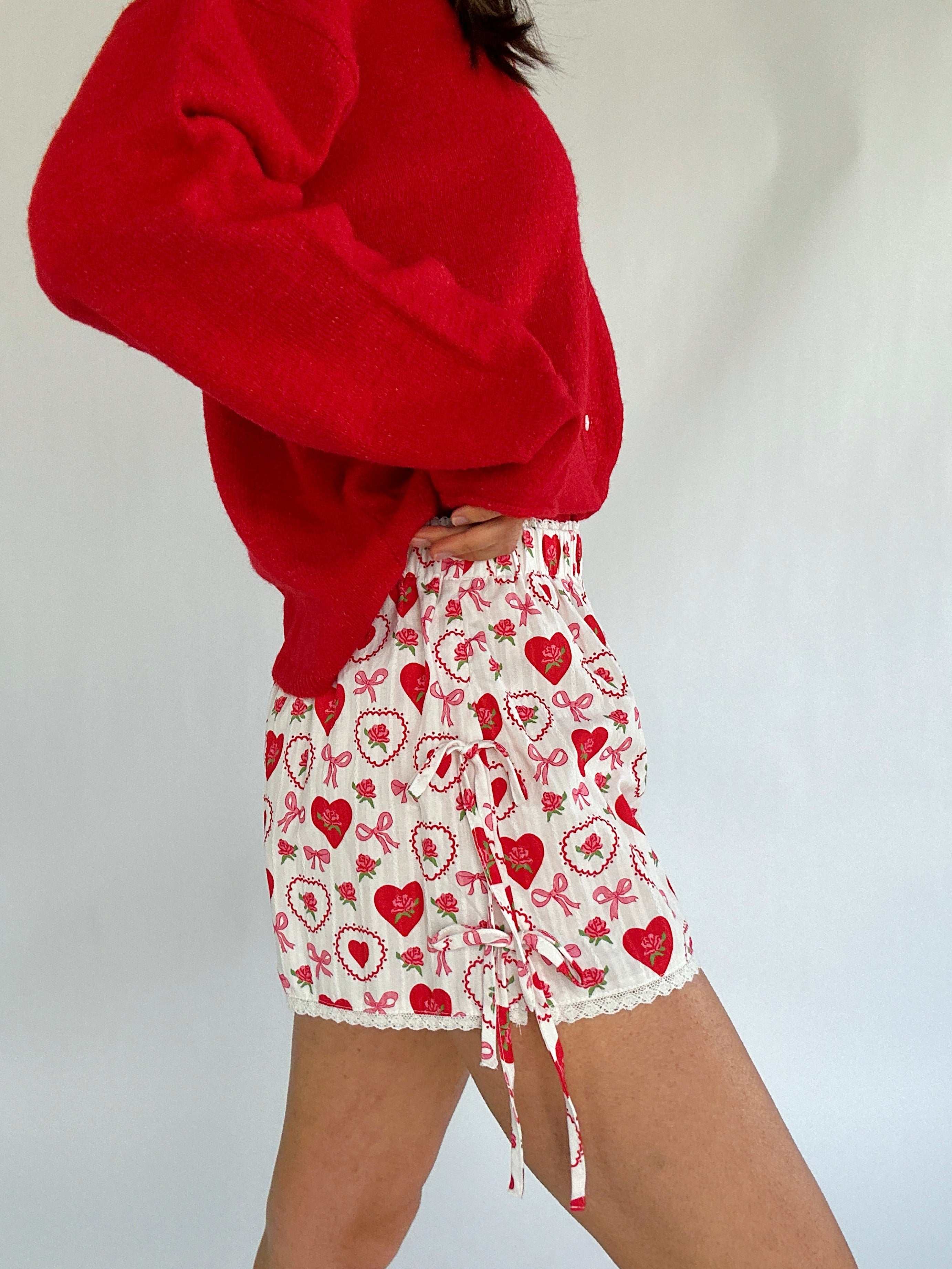 Person wearing a red cardigan and white shorts with red heart patterns on a plain background showing side details