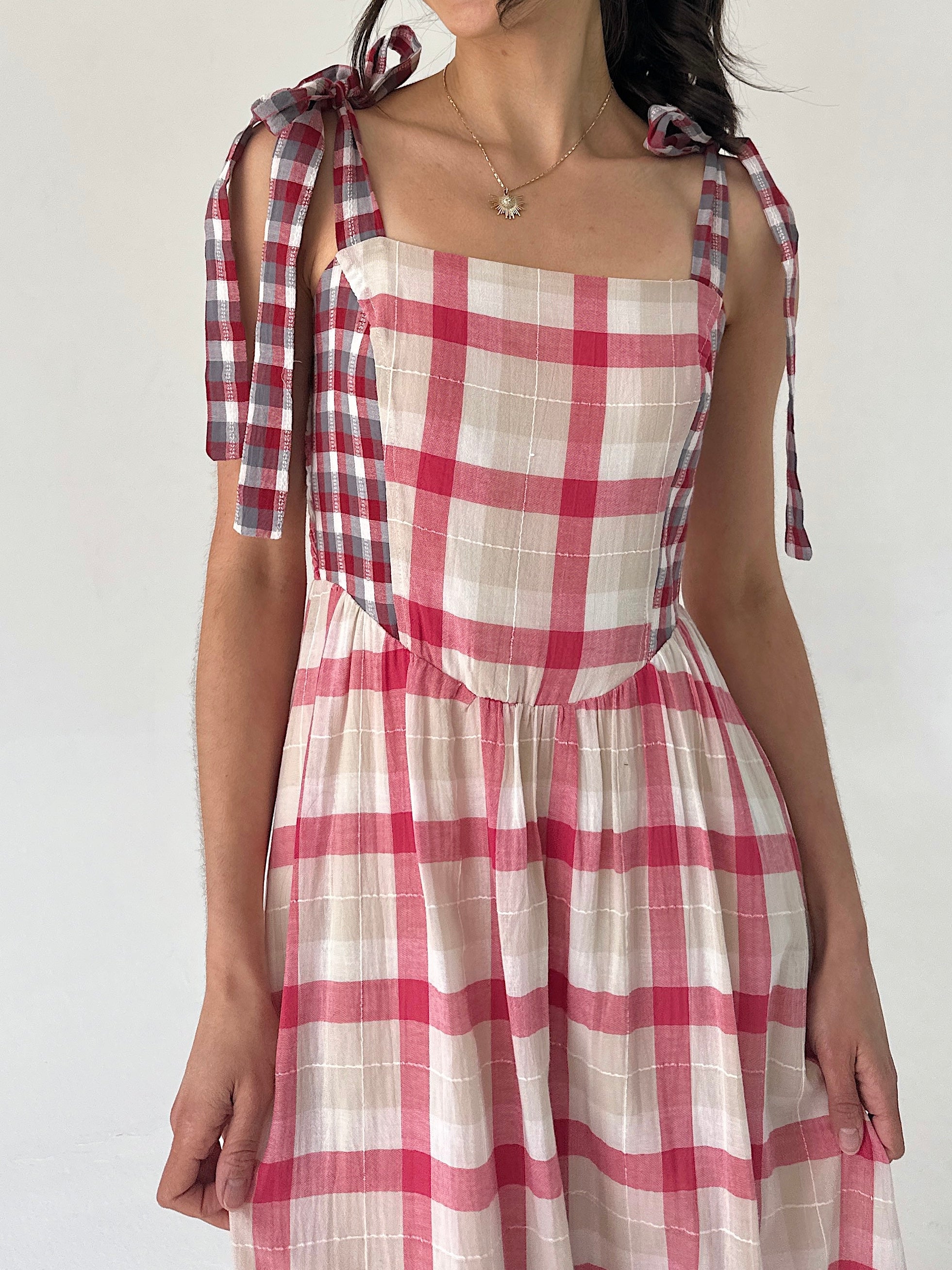 Red and white checkered dress with tied sleeves on a plain background