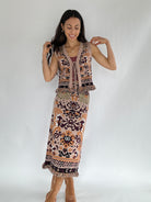 Woman wearing a boho patterned knit vest with tie front and matching knit skirt with a plain background