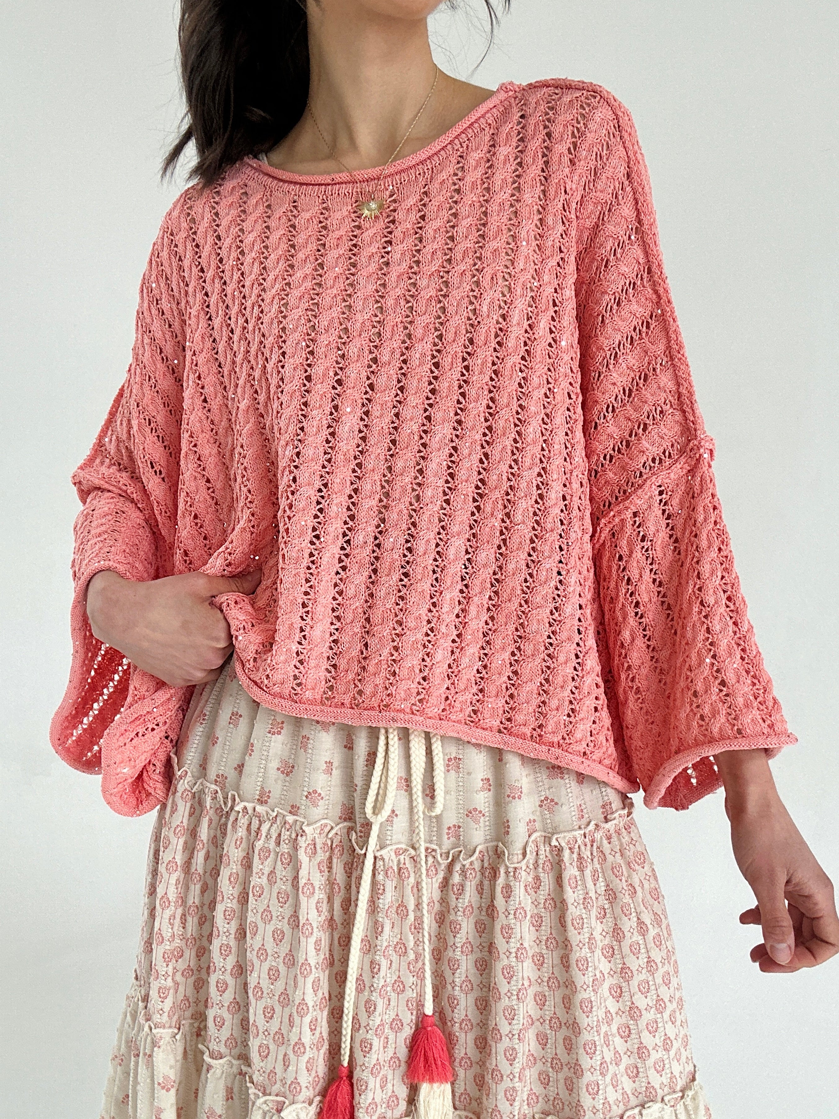 Person wearing a coral knitted sweater with a patterned skirt on a white background