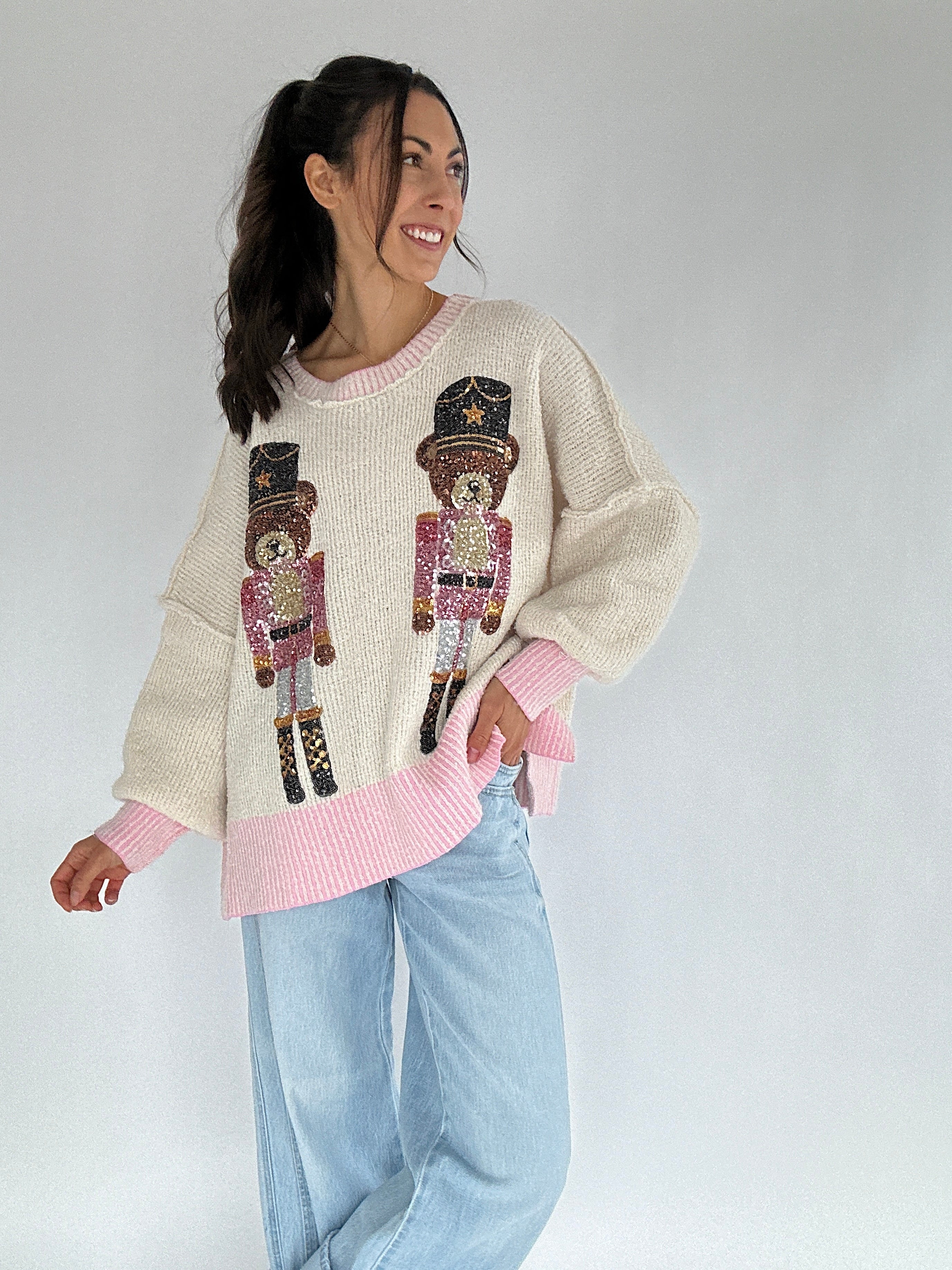 Woman wearing a cream sweater with sequin teddy nutcracker design on a plain background