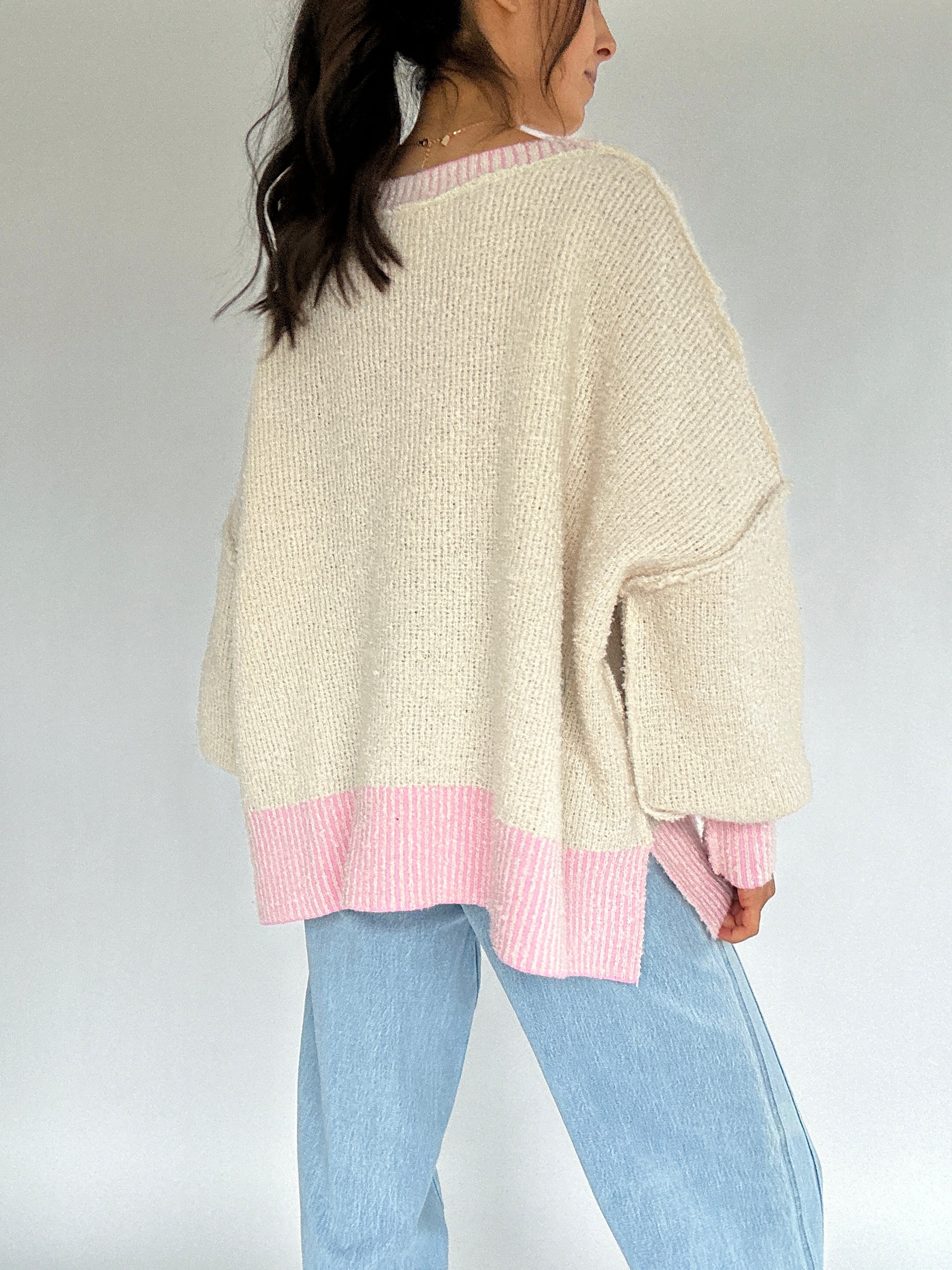 Person wearing a cream sweater with pink accents trim on a plain background to show back view