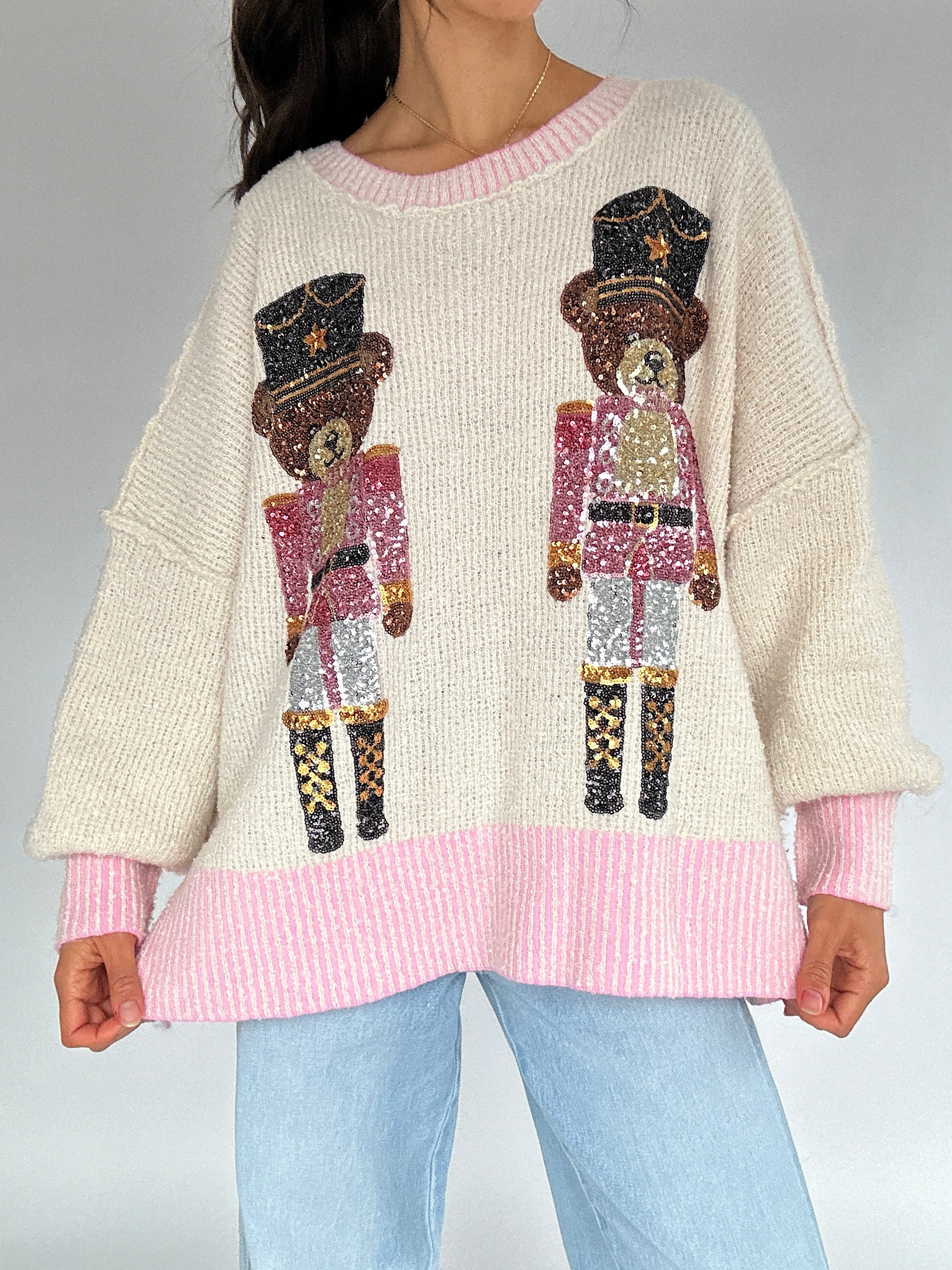 Person wearing a cream sweater with sequin teddy nutcracker designs on a plain background