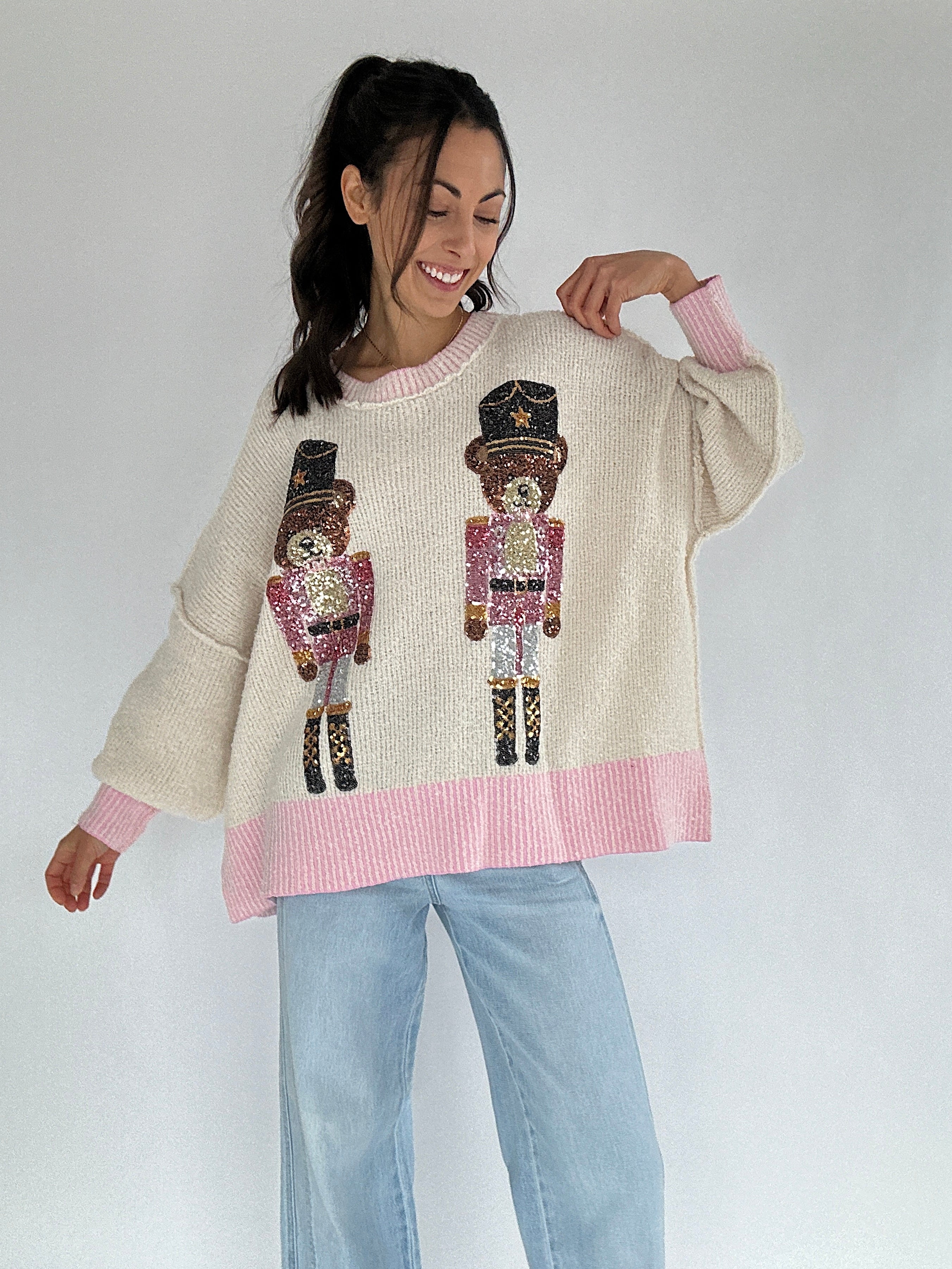 Woman wearing a cream sweater with sequin teddy nutcracker design on a plain background