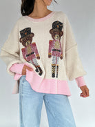 Person wearing a sweater with sequin teddy bear nutcracker designs and pink accents with an oversized fit