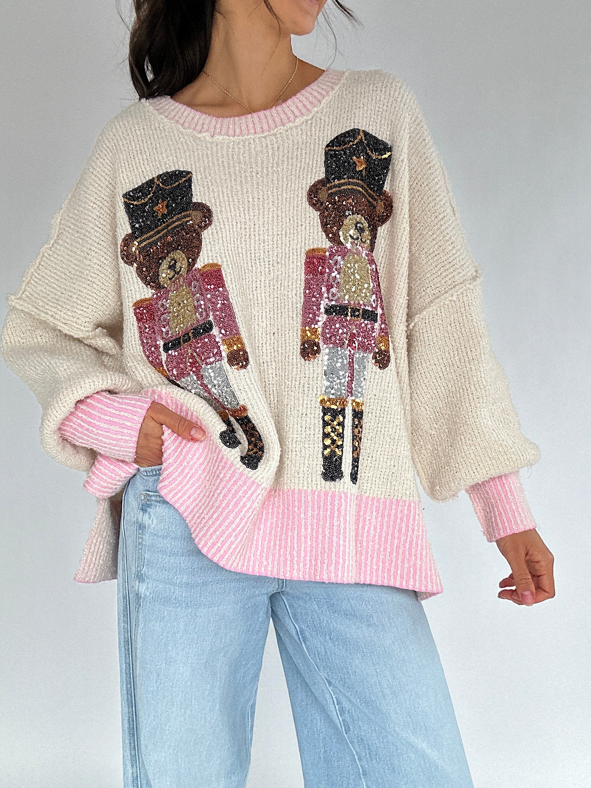 Person wearing a sweater with sequin teddy bear nutcracker designs and pink accents with an oversized fit