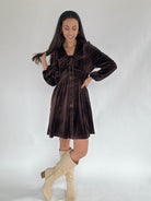 Woman wearing a brown velvet dress with peter pan collar and button front with beige knee-high boots on a white background