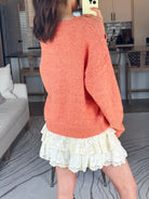 Person wearing an orange sweater and white skirt in a living room.