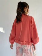 Person wearing a coral jacket and floral pants against a white background showing back