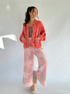 Woman wearing a coral jacket and pink patchwork patterned wide leg pants against a white background