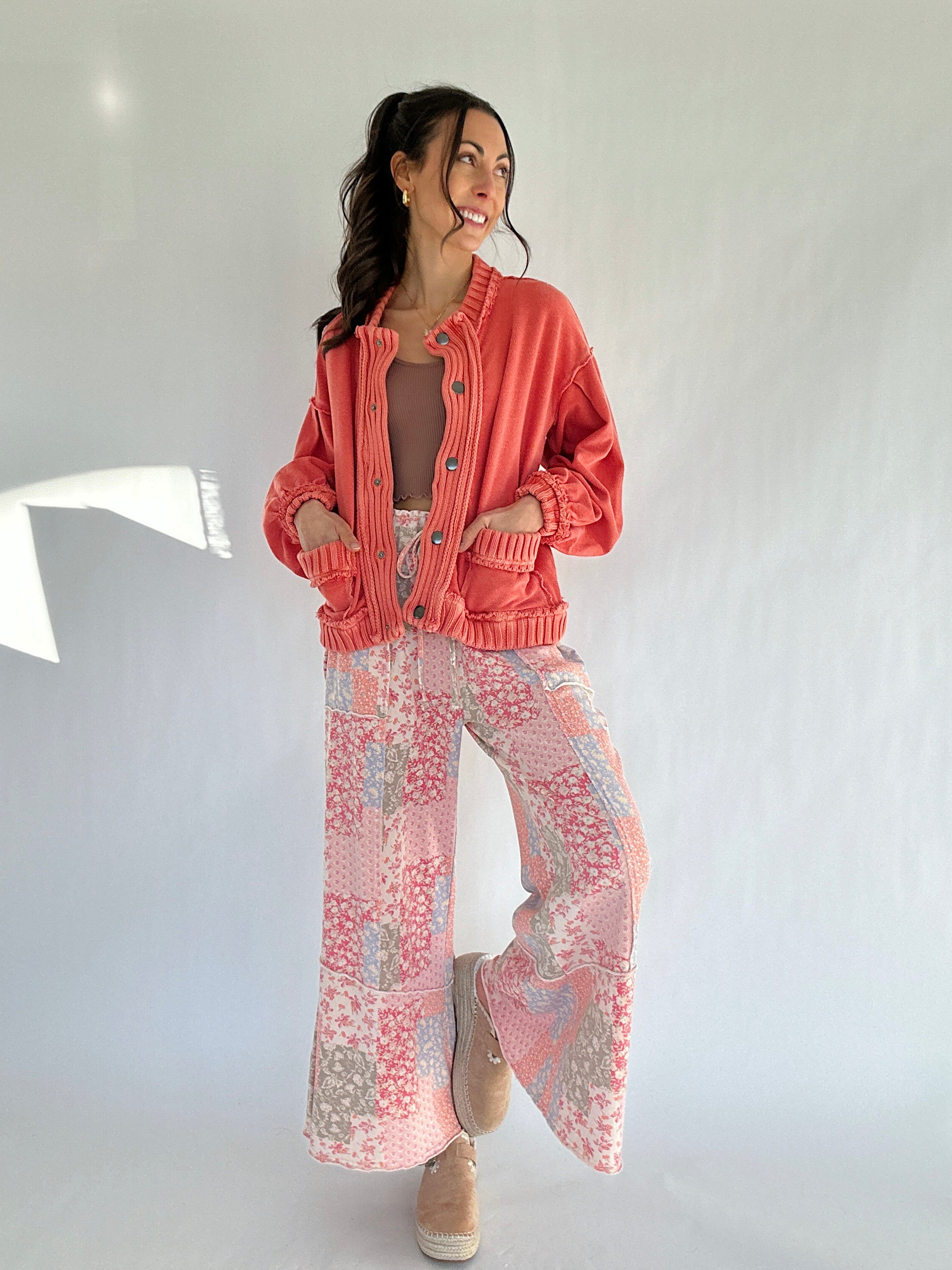 Woman wearing a coral jacket and pink patchwork patterned wide leg pants against a white background