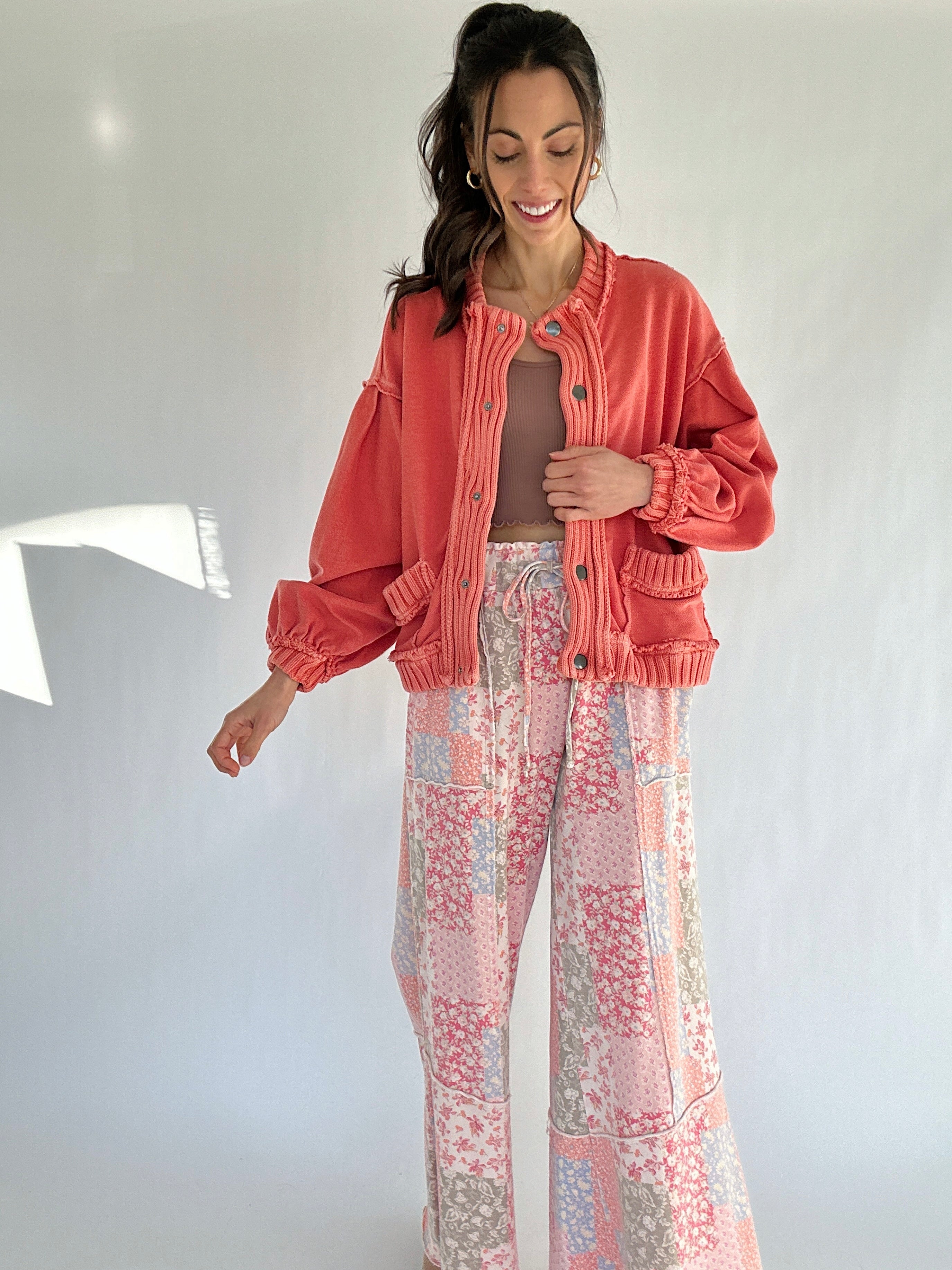 Woman wearing a coral jacket and patterned pants against a white wall