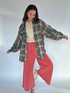 Woman wearing a green oversized plaid shirt and red wide leg sweatpants against a white background