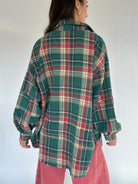 Person wearing a green plaid shirt with a white background showing back