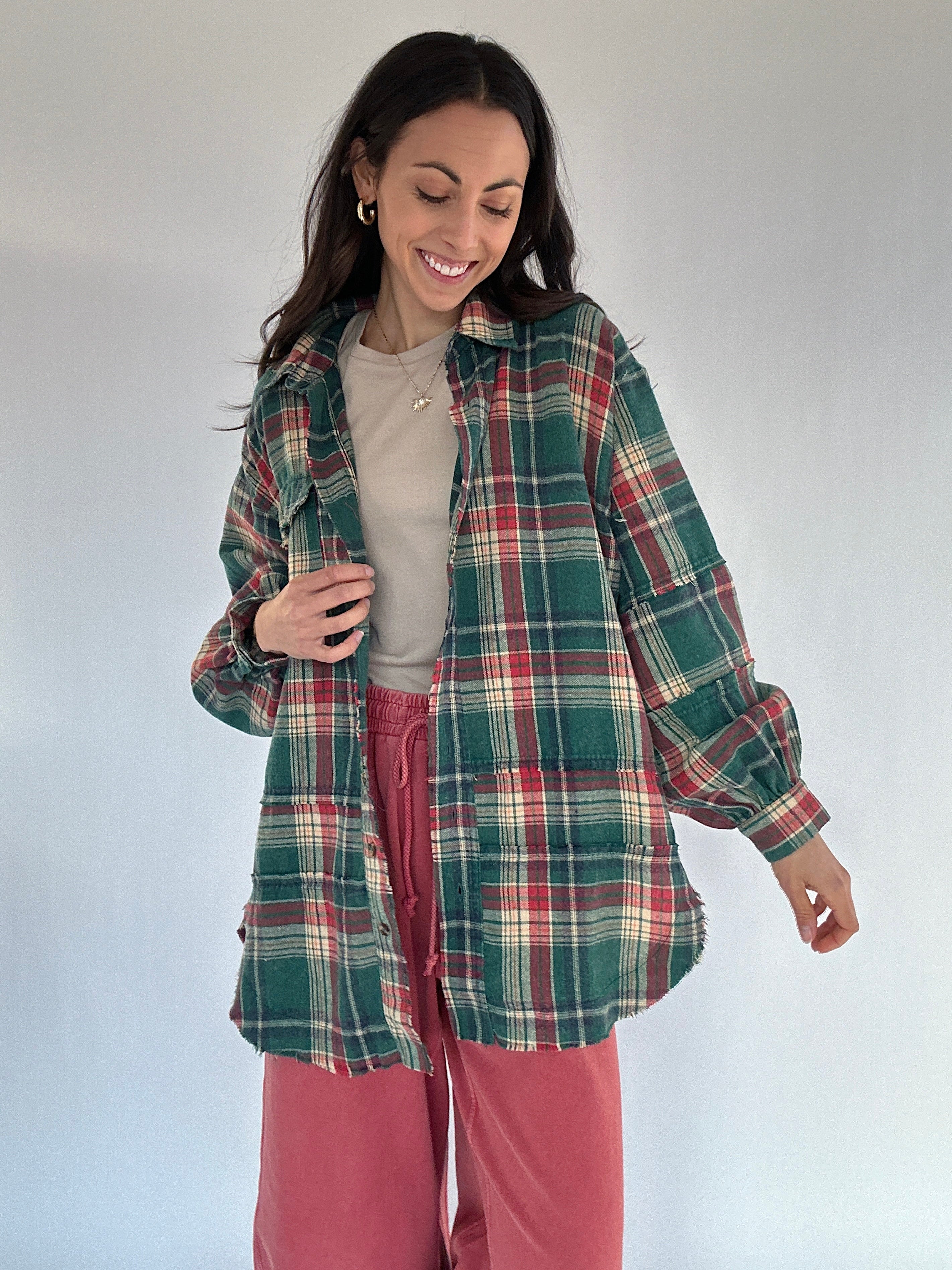 Woman wearing a green plaid shirt over a beige top and red pants on a white background