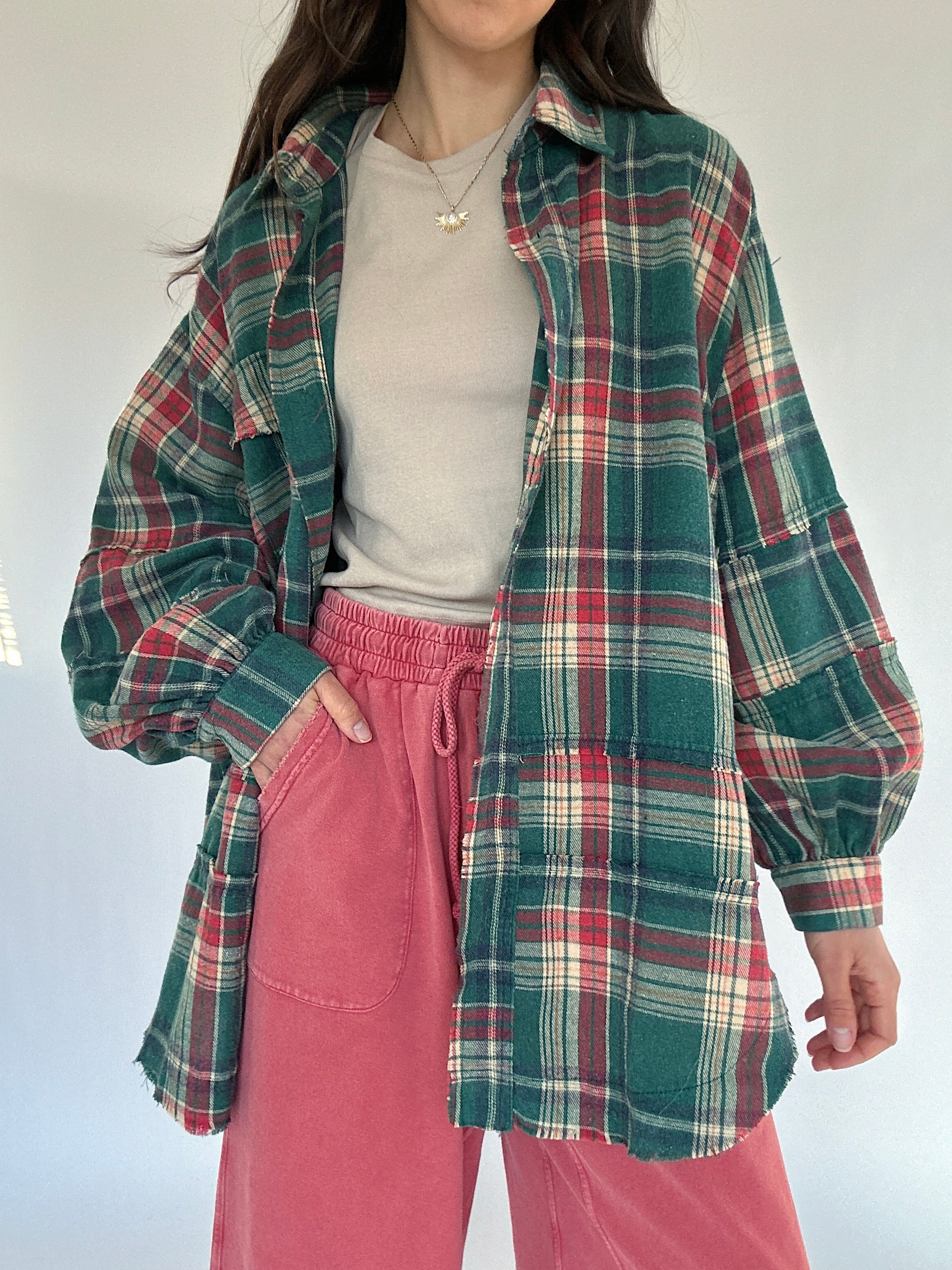 Person wearing a plaid shirt over a beige top and red pants against a white background