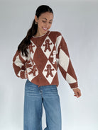 Woman wearing a brown and white patterned sweater with gingerbread men design on a plain background