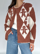 Person wearing a brown and white patterned cardigan with gingerbread men design on a plain background