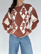 Person wearing a brown and white patterned sweater with gingerbread men design on a plain background