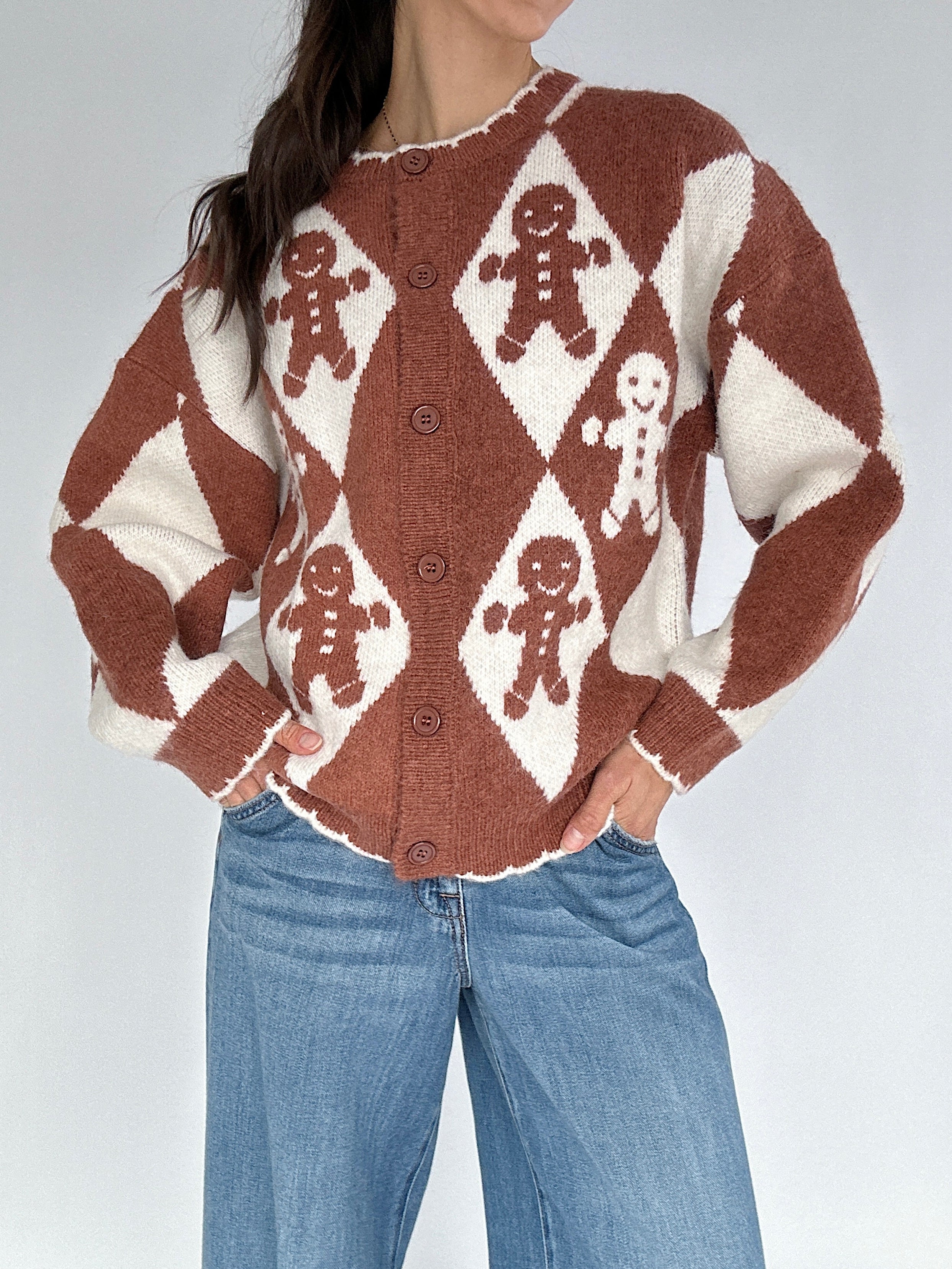 Person wearing a brown and white patterned sweater with gingerbread men design on a plain background
