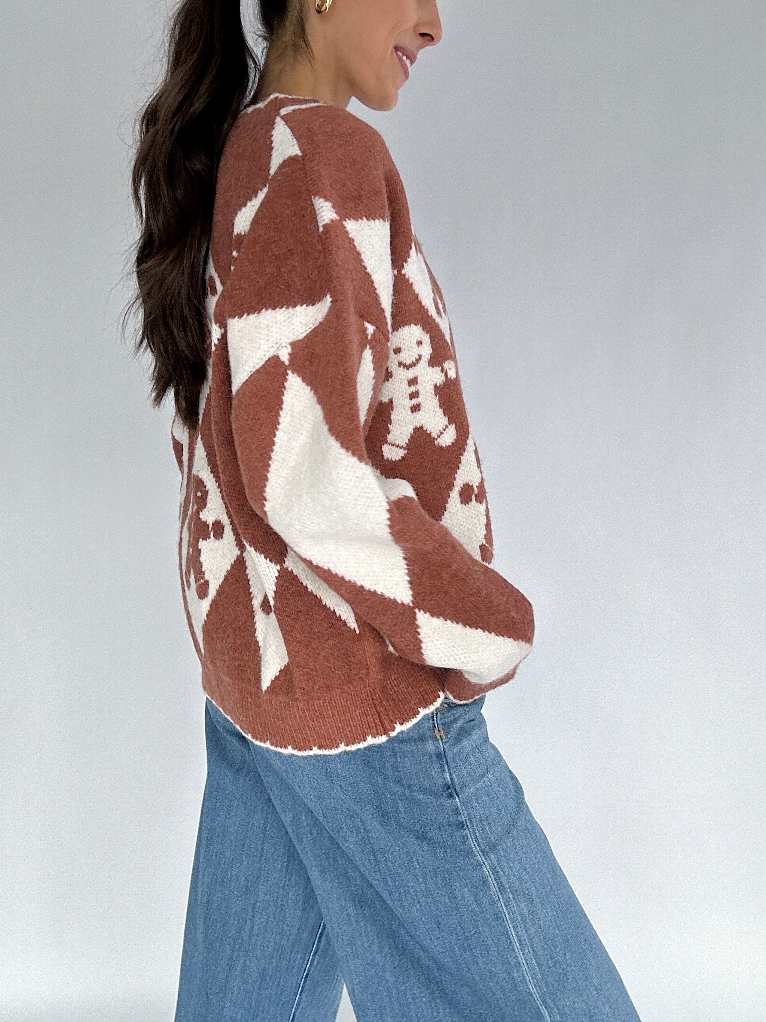 Person wearing a brown and white patterned sweater with blue jeans on a plain background