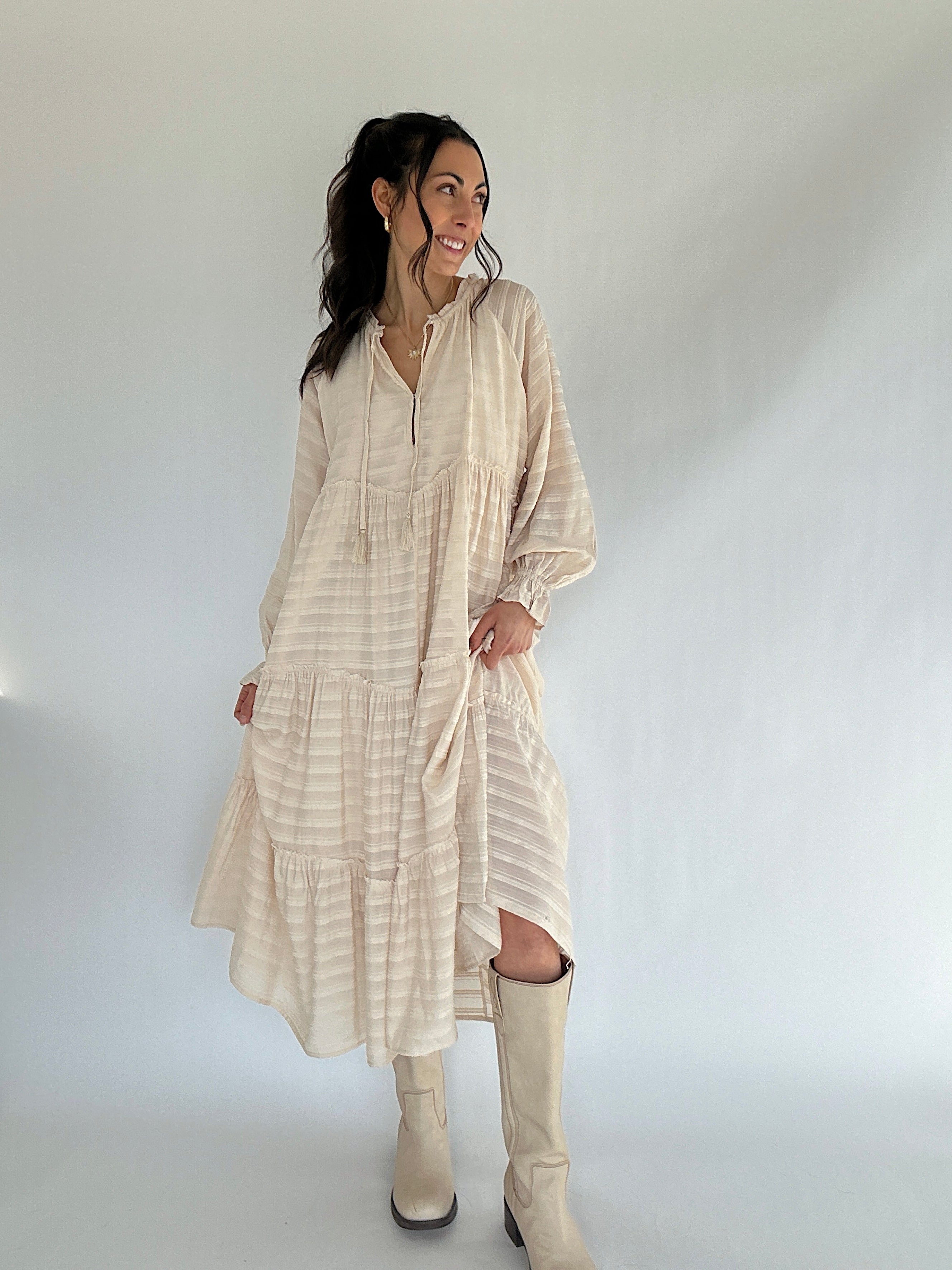 Woman wearing a beige dress and boots against a white background