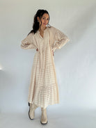 Woman wearing a beige dress with long sleeves against a white background