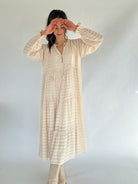 Woman wearing a long, beige-colored dress against a plain background